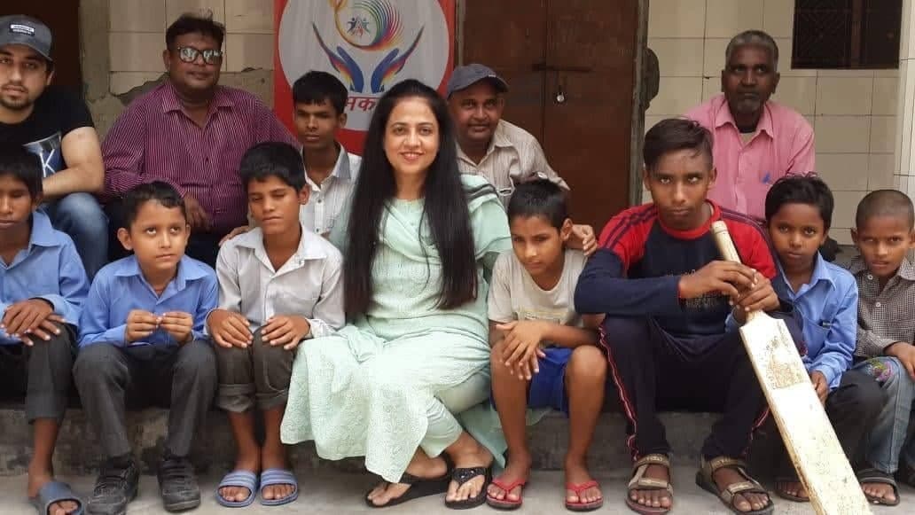 Shubhkarman volunteers seated with a group of children in front of the Shubhkarman banner